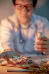 Male Asian doctor showing pills on his hand. Doctor working with medicine paperwork on the desk in clinic or hospital. Medical treatment and health care concepts.