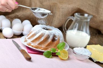 Woman sprinkles a homemade lemon bundt cake with sugar, lemon, melissa, milk, eggs and butter