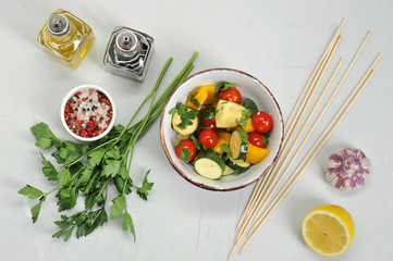 Tomatoes, zucchini, sweet peppers are marinated with garlic, parsley, olive oil, balsamic sauce and lemon. In the frame, a bowl of vegetables and marinade products. View from above. White background.