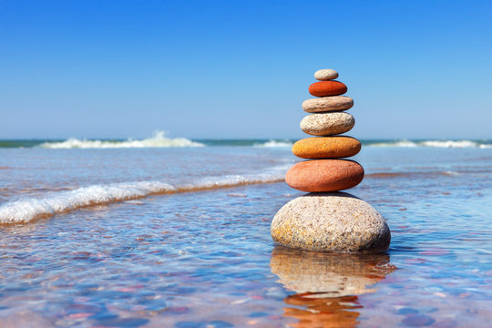 Rock zen pyramid of colorful pebbles standing in the water on the background of the sea. Concept of balance, harmony and meditation.