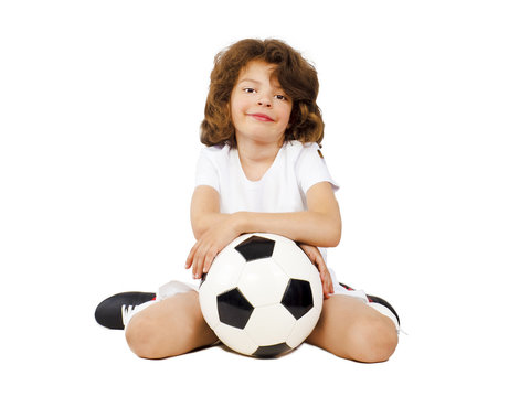 Photo of smiling preschool boy in sportswear leaning on a soccer ball - posing on studio. Isolated on white