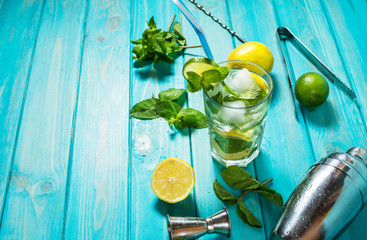 Mojito cocktail with lime and mint in highball glass on a wood table. Blue background.