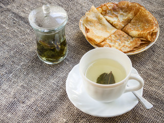 A cup of tea and a plate with pancakes on a rustic sacking