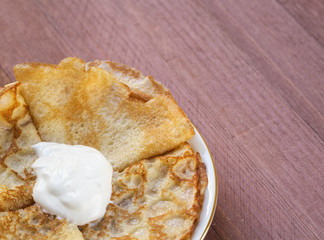 Plate with hot pancakes with sour cream on a wooden background