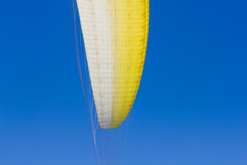 A wing of a paraglider against a clear blue sky.