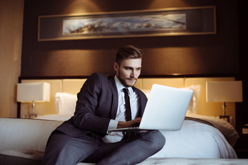 Young handsome businessman talks on-line with his business partners at the hotel room. Hotel service. Booking hotel. Freelancer sitting on his sofa in a hotel room and working with his computer. 