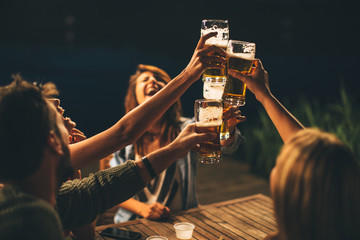 Group of friends drink beer on the terrace and toast during summer night - Powered by Adobe