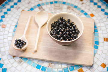 A plate of black currant and a wooden spoon on a table.