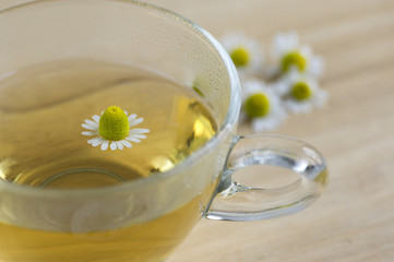 Matricaria chamomilla flowers and trasparent cup of tea on wooden table, fresh flowering herbal...