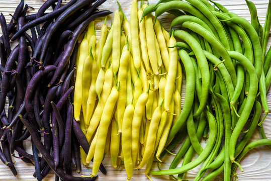 Collection of green, yellow and purple bush beans, opened green peas on wooden background