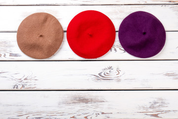 Top view womens hats. Brown, red and purple berete hats. White wooden desk background.