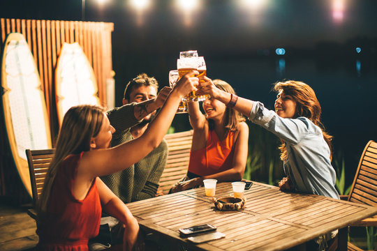 Group of friends drink beer on the terrace and toast during summer night