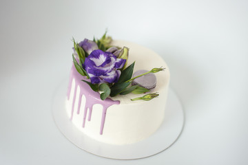 Fototapeta na wymiar White sponge cake with violet flowers on a white background