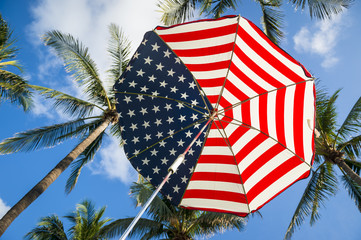 Stars and stripes USA flag sun umbrella below tropical green coconut palms and tropical sky