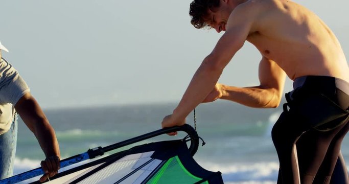 Male surfer preparing windsurfer in the beach 4k