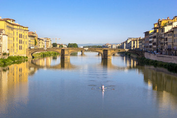 Fototapeta premium Panoramic view of the Arno River and stone medieval bridge Ponte Vecchio with beautiful reflection of colorful houses and small boat, Florence, Tuscany, Italy.