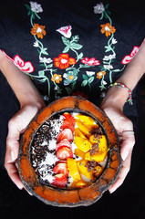 Eating healthy breakfast bowl. Female hands hold a bowl of coconut with smoothie bowl of fresh strawberries, mango, granola, chia seeds, coconut shavings. Dieting, vegetarian, vegan food concept.