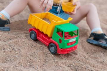 A child plays with a toy car. A child plays with a car in the sandbox