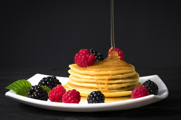 .pancakes with honey blackberries and raspberries on a black background