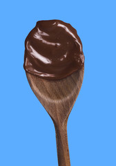 Melted dark chocolate wood spoon isolated on blue background.