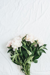 Flat lay, top view of white peonies flower bouquet on white blanket background. Minimal summer floral concept.