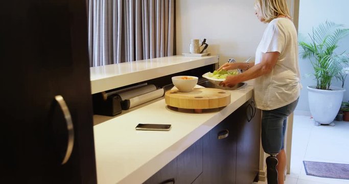 Woman with prosthetic leg washing and cutting vegetables 4k