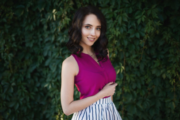 Fototapeta premium Emotive portrait of young brunette woman with bright fashionable makeup posing over green foliage.