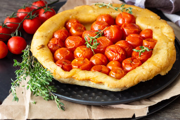 Homemade tart with cherry tomatoes of puff pastry with raw tomatoes and thyme on  dark wooden background. Tomatoes tart tatin. Rustic style.