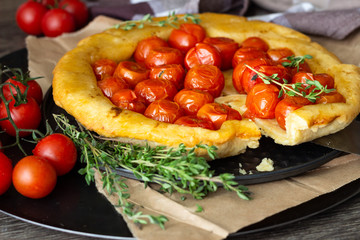 Homemade tart with cherry tomatoes of puff pastry with raw tomatoes and thyme on  dark wooden background. Tomatoes tart tatin. Rustic style.