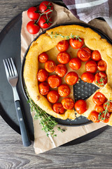 Homemade tart with cherry tomatoes of puff pastry with raw tomatoes and thyme on  dark wooden background. Tomatoes tart tatin. Rustic style.