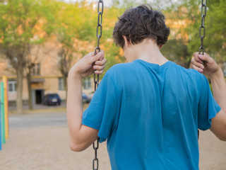back view of young boy sitting on a swing on a summer day