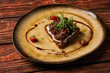 Fresh Bruschetta with lamb beef. Open sandwich with Dark rye bread, dried cherry tomatoes, rosemary, olives and arugula on plate at luxury restaurant table, top view. Delicious snack food