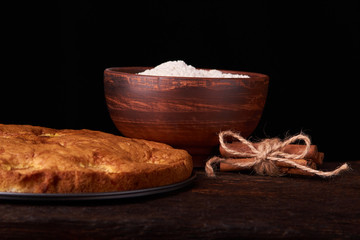 Fototapeta na wymiar On a dark wooden table, fashionable bakeries, a bowl with flour, apricot cake and tools stand on table