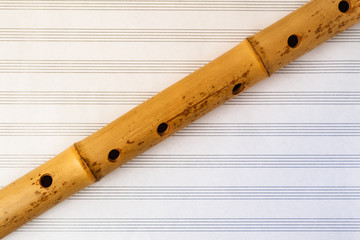 Naklejka premium Simple wooden flute on a background of pure sheet music