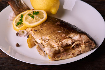 Appetizing baked fish, covered with juicy lemons, garlic and salt on side, above view