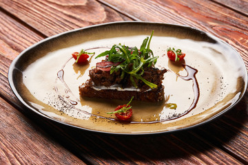 Fresh Bruschetta with lamb beef. Open sandwich with Dark rye bread, dried cherry tomatoes, rosemary, olives and arugula on plate at luxury restaurant table, top view. Delicious snack food