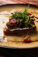 Fresh Bruschetta with lamb beef. Open sandwich with Dark rye bread, dried cherry tomatoes, rosemary, olives and arugula on plate at luxury restaurant table, top view. Delicious snack food