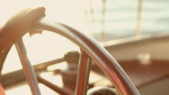 man is spinning the metallic wheel of the boat. sunset reflects on clear calm water.