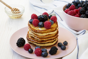 Pancakes with berries and honey on a pink plate, low angle. Closeup.