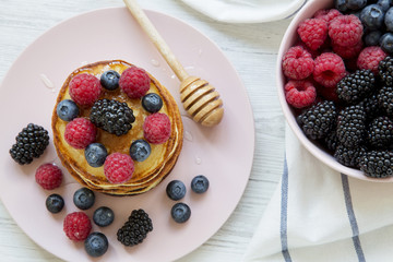 Top view, pancakes with berries and honey on a pink plate, bowl of berries. Closeup. Flat lay, overhead, from above.