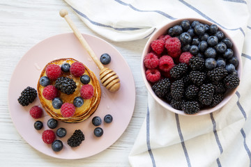 Pancakes with berries and honey on a pink plate, bowl of berries, top view. Closeup.