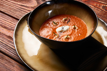 Tomato soup with shrimp. Seafood creamy soup with goat cheese, olive powder, wild shrimps on bowl plate at wooden table, top view, close-up. Delicious vegetarian diet food.