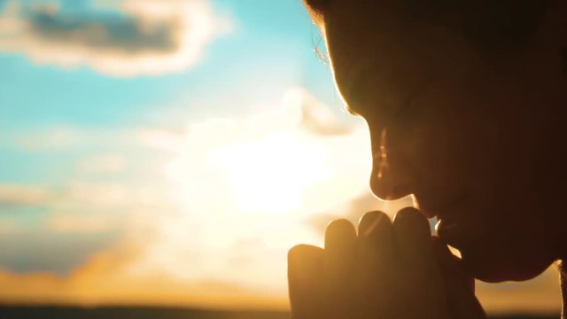 girl praying. girl folded her hands in prayer silhouette at sunset. slow motion video. Girl folded her hands in prayer pray to God. asks forgiveness for lifestyle sins of repentance. believing girl