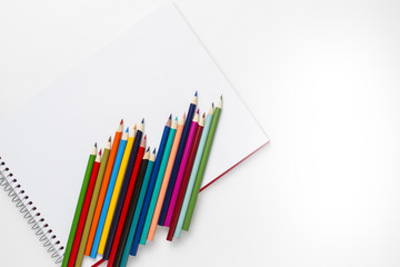 Drawing notebook and colored pencils on white table