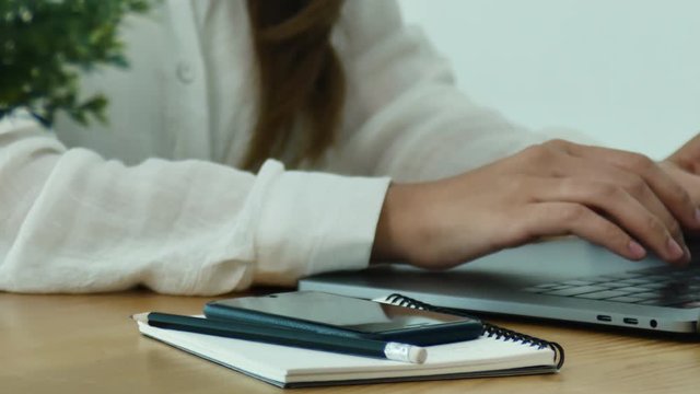 Beautiful young smiling asian woman working on laptop while sitting in a living room at home. Asian business woman using phone for work in her home office. Enjoying time at home.