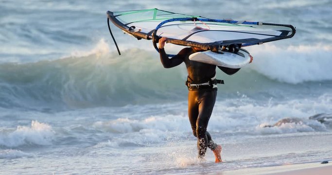 Male surfer carrying windsurfer in the beach 4k
