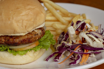 Tasty burger with salad on white plate, snack food closeup. Hamburger close-up photo. Rich nutritive breakfast.