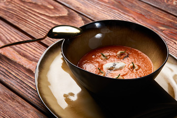 Hot Tomato soup with shrimp. Seafood creamy soup with goat cheese, olive powder, wild shrimps on bowl plate at wooden table, top view, close-up. Delicious vegetarian diet food.