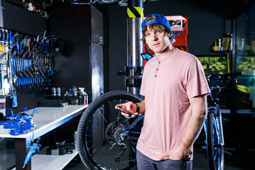 A young, stylish redheaded male small business owner selling and repairing a bike is wearing a blue...