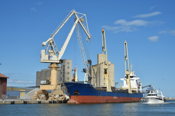 Fototapeta na wymiar Les grues du port de commerce de Port-la-Nouvelle, Aude, Languedoc, Occitanie, déchargent un bateau.
